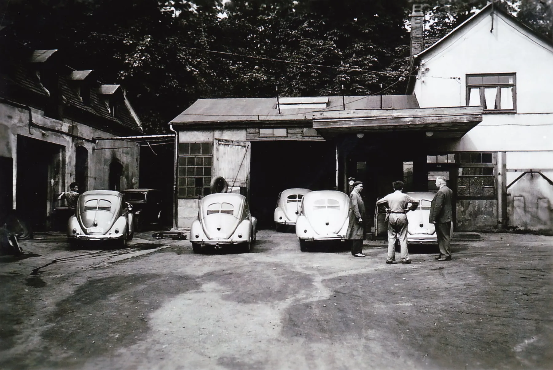 Werkstatthof mit mehreren VW Käfern vor den Garagentoren, davor Mitarbeiter